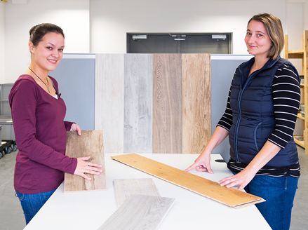Zwei Mitarbeiterinnen zeigen verschiedene Fliesen in Holzoptik