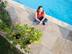 Frau sitzt auf Sandsteinterrasse am Pool von oben fotografiert