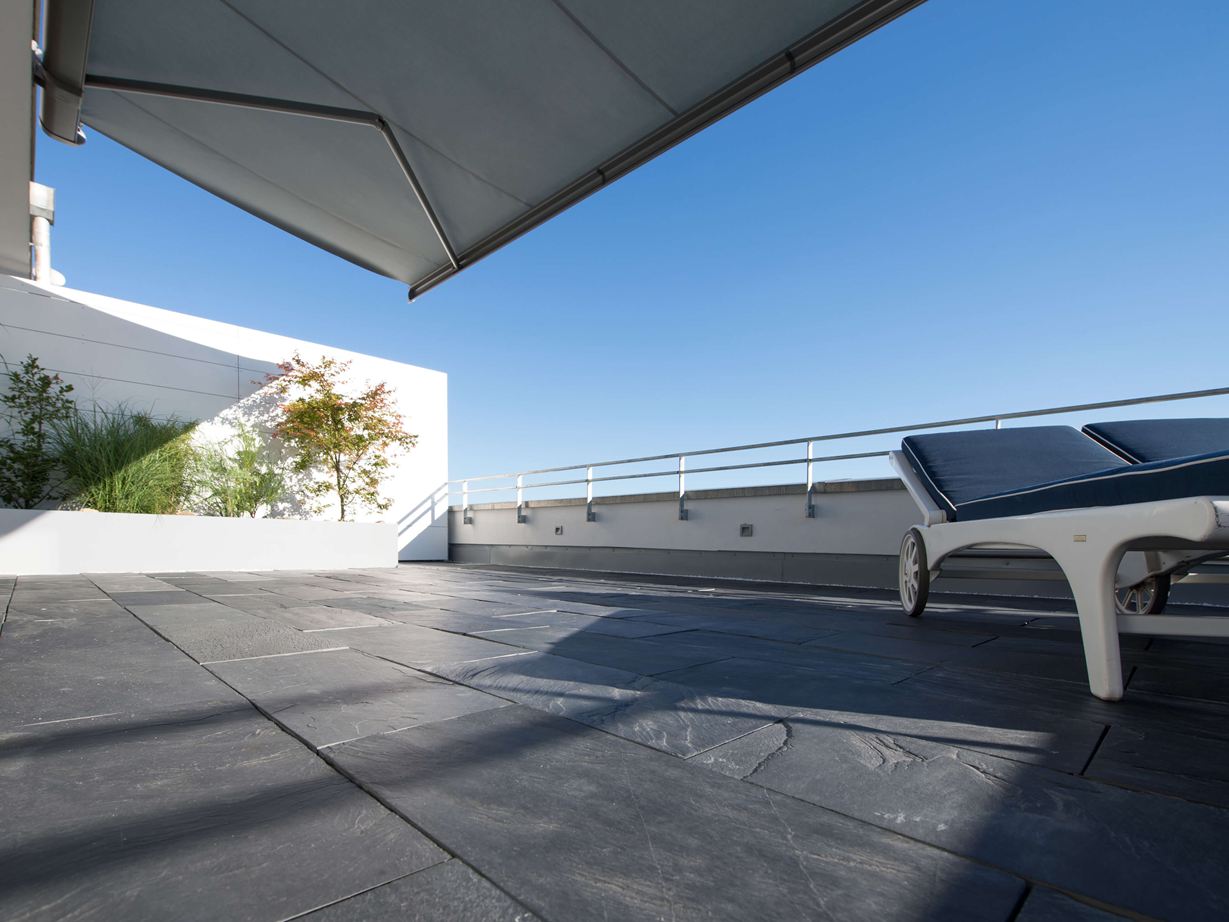 Praktisch: schwarzer Schiefer ist wärmespeichernd Dachterrasse mit Schiefer als Bodenbelag und Liegestühlen am Rand aus der Froschperspektive