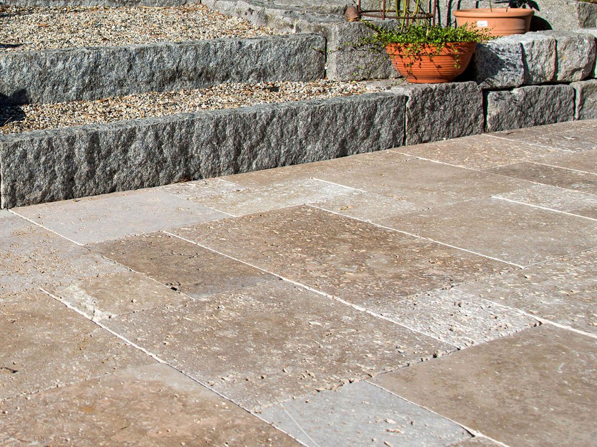 Travertin Noce: passt gut zum Landhausstil Terrasse mit Natursteinplatten aus braunem Travertin, im Hintergrund eine Treppe mit Granitsteinen