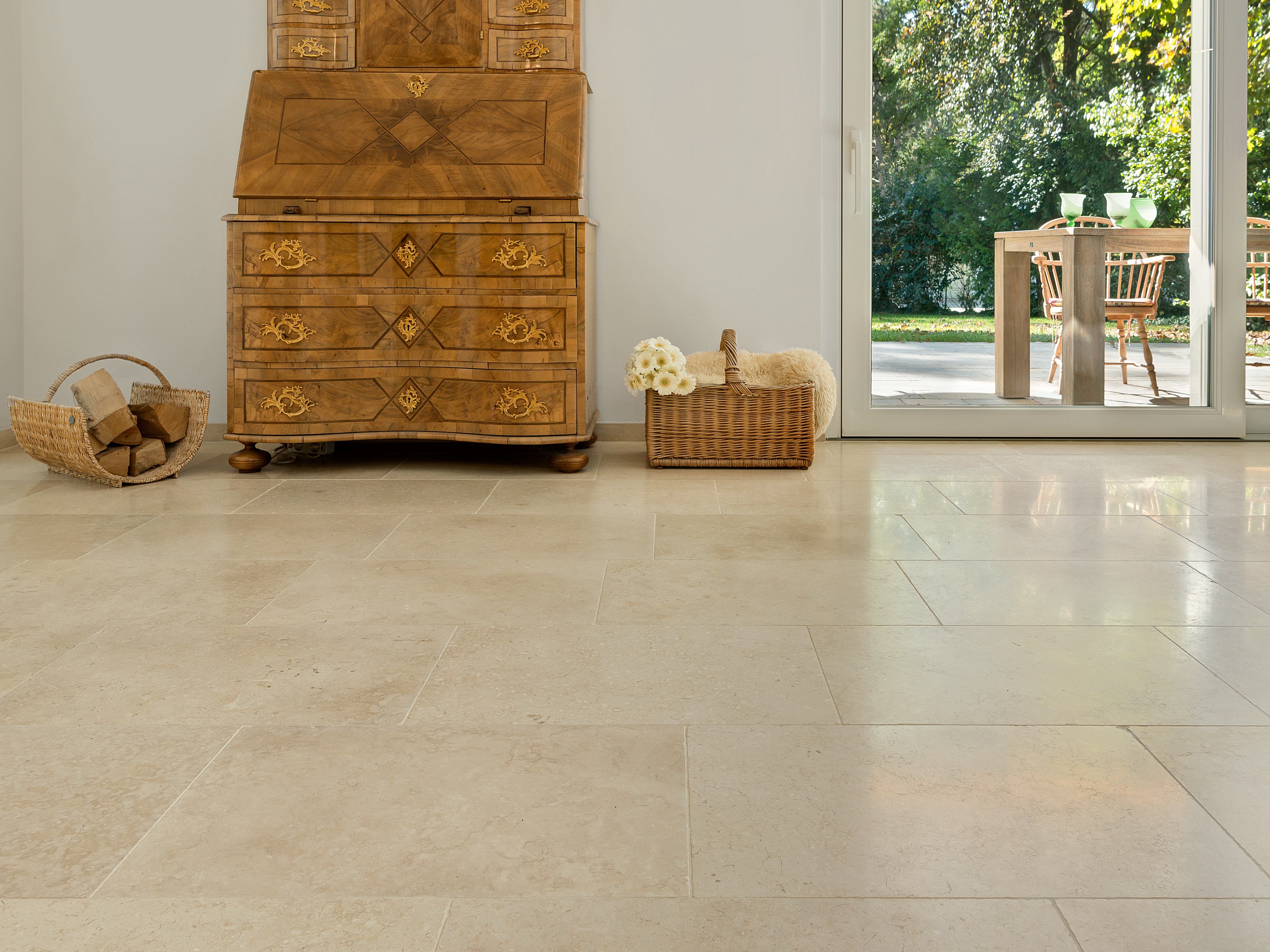 Harmonische Beigetöne: Kalksteinfliese Cleopatra Light Antiker Holzschrank auf hellen Kalksteinfliesen Cleopatra Light, im Hintergrund Blick auf die Terrasse und den Garten