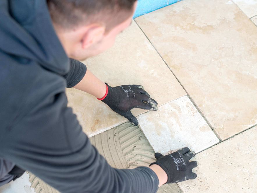 Mann verlegt Travertinfliesen in hellem Beige im Römischen Verband