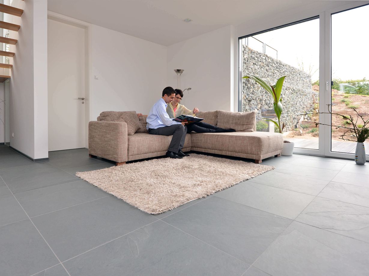Grey Slate wirkt großzügig und modern. Grossformatige Schieferfliese Grey Slate im Wohnzimmer mit heller Couch und weissen Wänden. Ein Paar sitzt auf der Couch