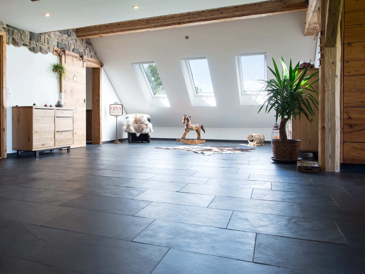 Der anthrazitfarbene Schiefer wirkt trendy. Raum mit anthrazitfarbenem Schieferboden und Holzmöbeln, weisse Wände