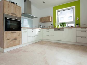 Küche in Weiss mit Holzelementen und grüner Fensterumrahmung auf Travertinfliese Light mit getrommelter, ungespachtelter Oberfläche