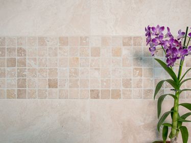 Orchidee vor Mosaik-Wand mit hellem Travertin