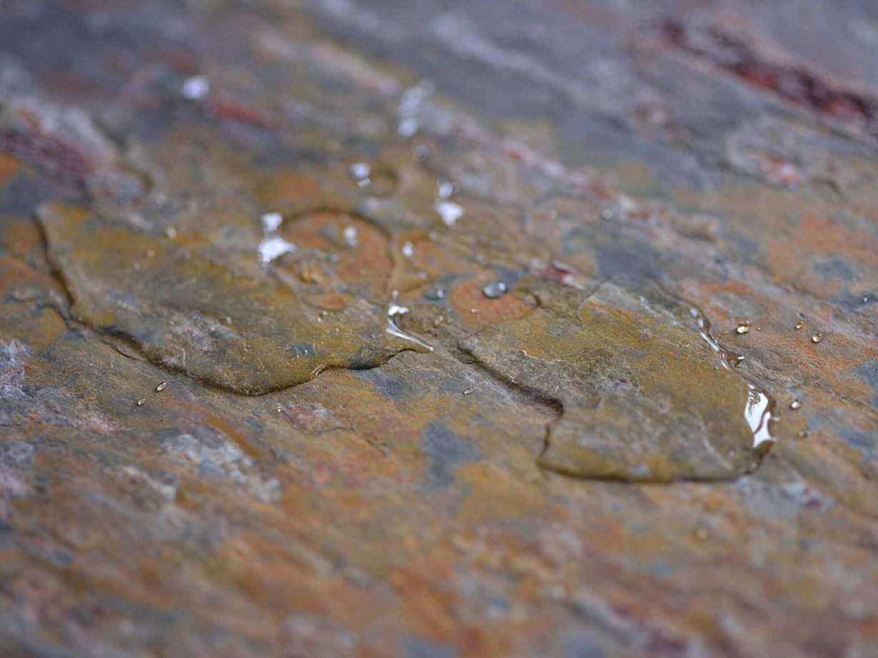 Nahaufnahme von Natursteinfliese mit kleiner Wasserlache auf der Oberfläche