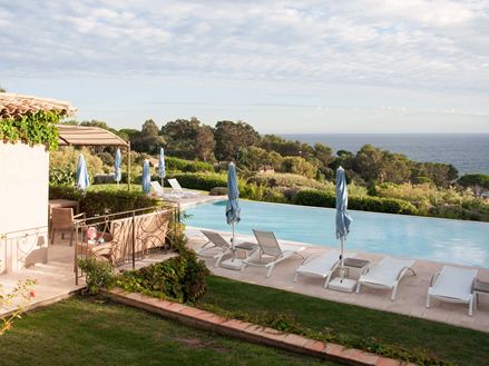 Ein Pool mit weißen Liegen und Travertinplatten, im Hintergrund das Meer