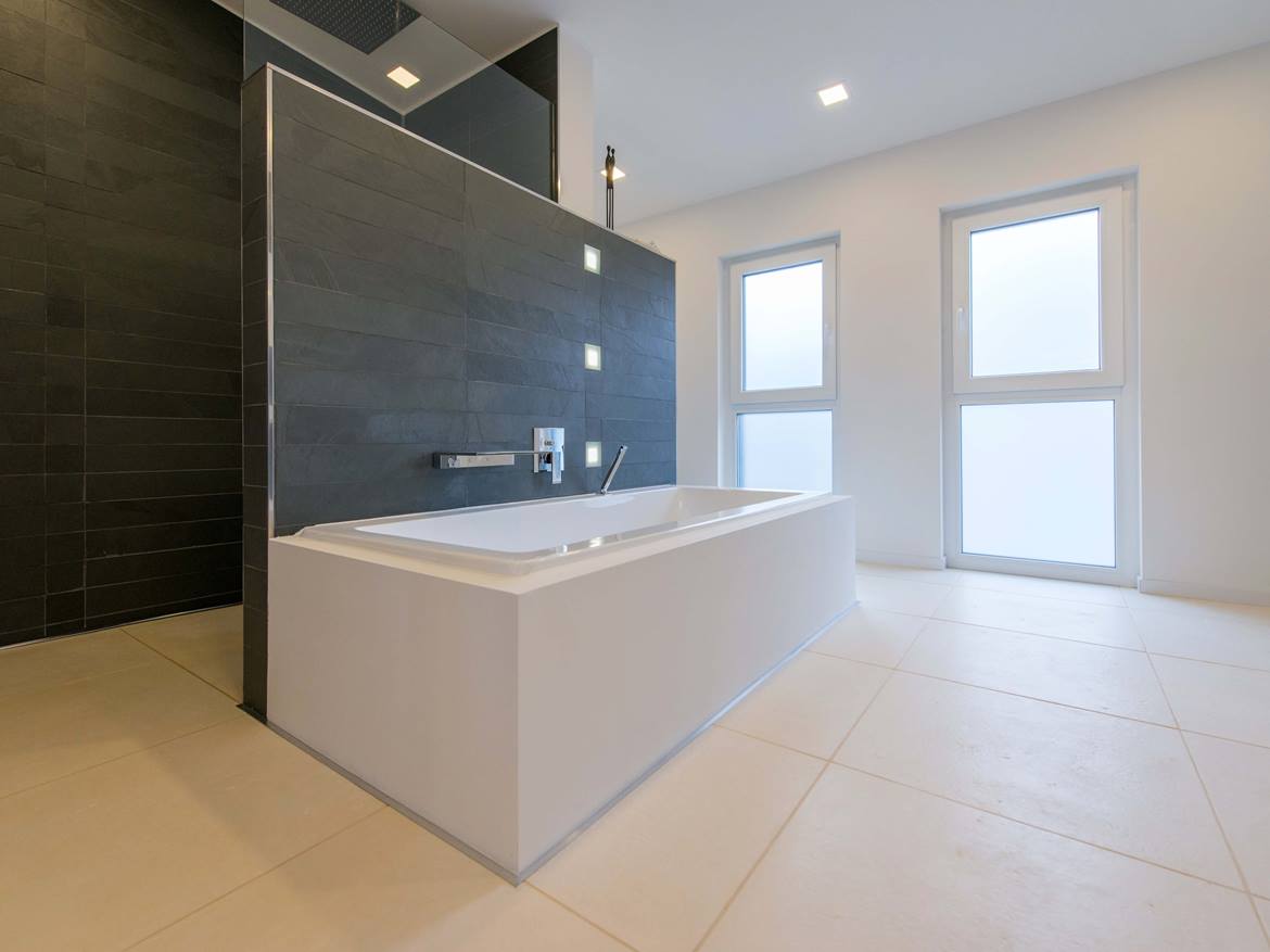 Badewanne mit Wandverkleidung aus Schiefer im Hintergrund und gebuersteter Kalksteinfliese auf dem Boden