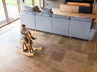 Kind sitzt auf Schaukelpferd und spielt im Wohnzimmer mit Travertinboden Noce SELECT