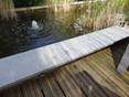 Ein Teich im Halbschatten, davor Holzdielen und Granitplatten als Teichrand