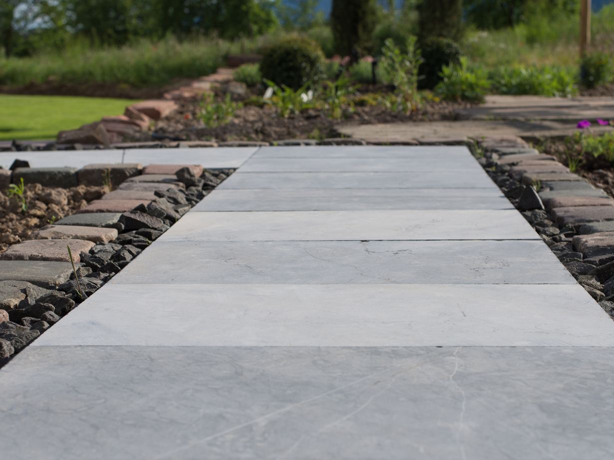 Blausteinplatten als Gartenweg, daneben Beete und im Hintergrund ein grüner Rasen