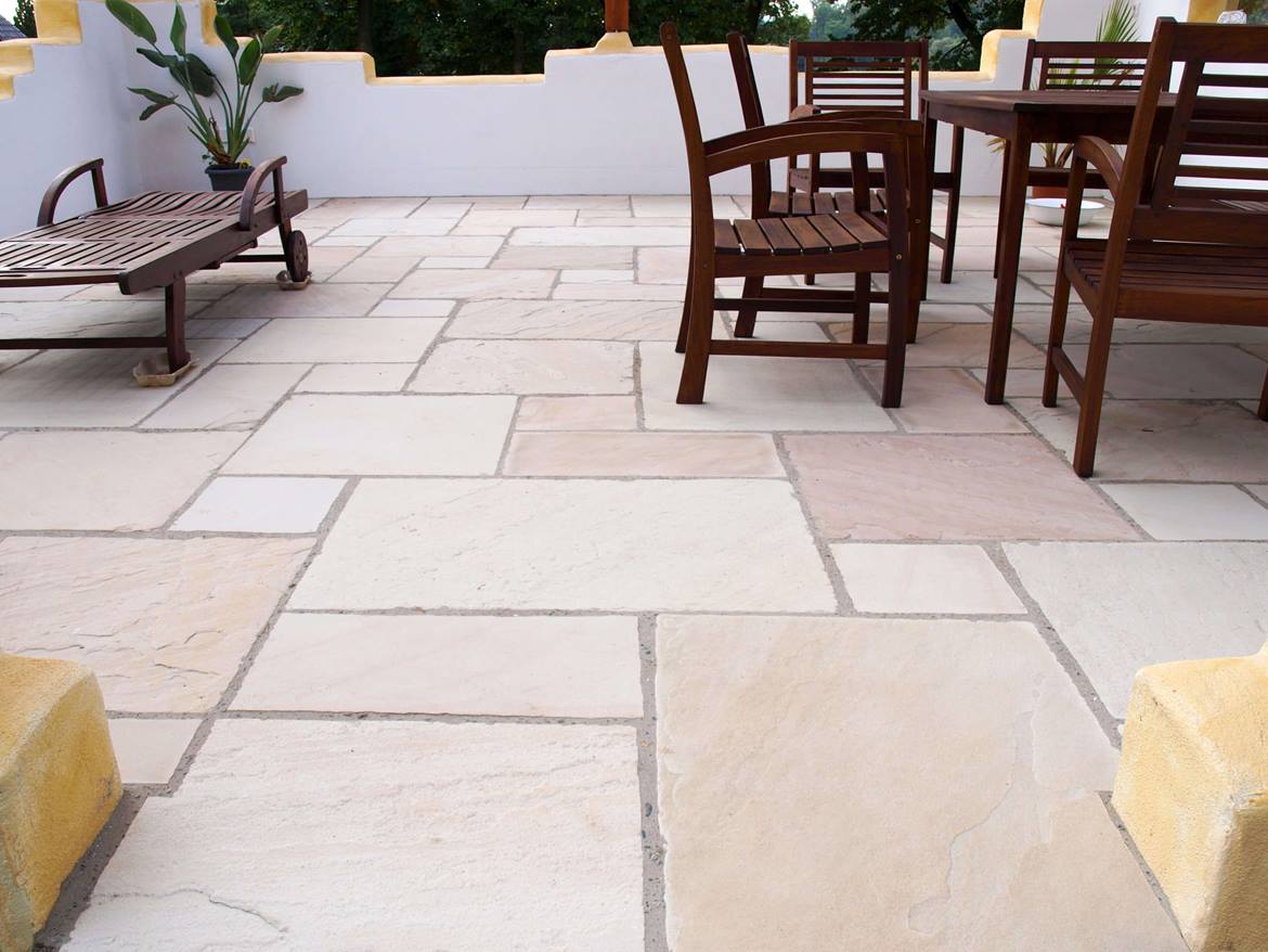 Terrasse mit dunkelbraunem Holztisch, dunkelbraunen Holzstühlen und Sandsteinplatte Yellow Mint als Bodenbelag