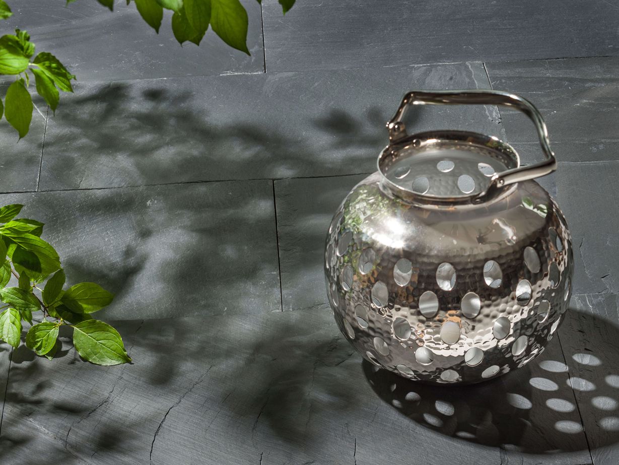 Metallener Teelichthalter und grüne Blätter auf verlegter Schieferplatte Black Rustic