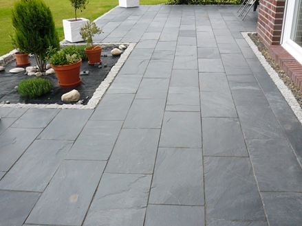 Terasse mit Topfpflanzen und Schiefer Black Rustic als Bodenbelag, rechts ist eine Hauswand aus Backsteinen zu sehen