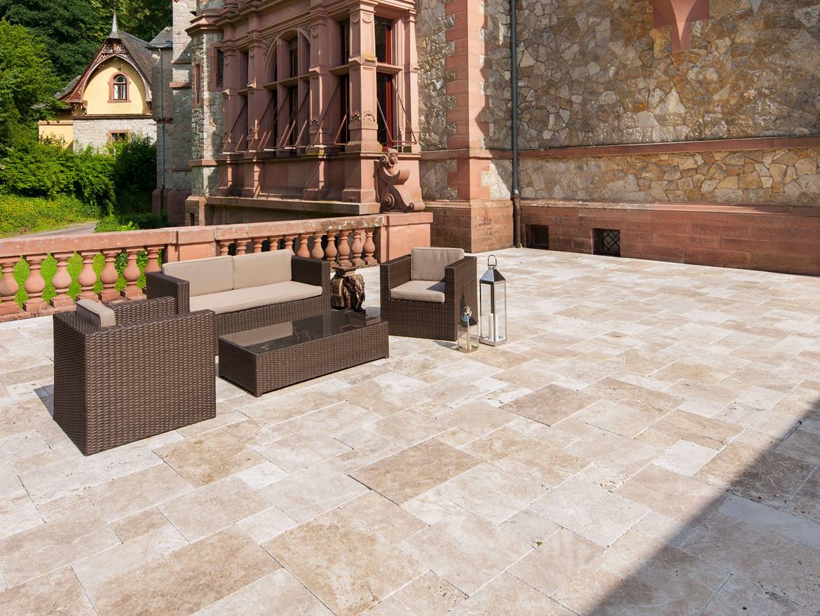 Terrasse mit Gartenmöbeln und Natursteinwand im Hintergrund, Bodenbelag: Travertin Medium mit getrommelter Oberfläche