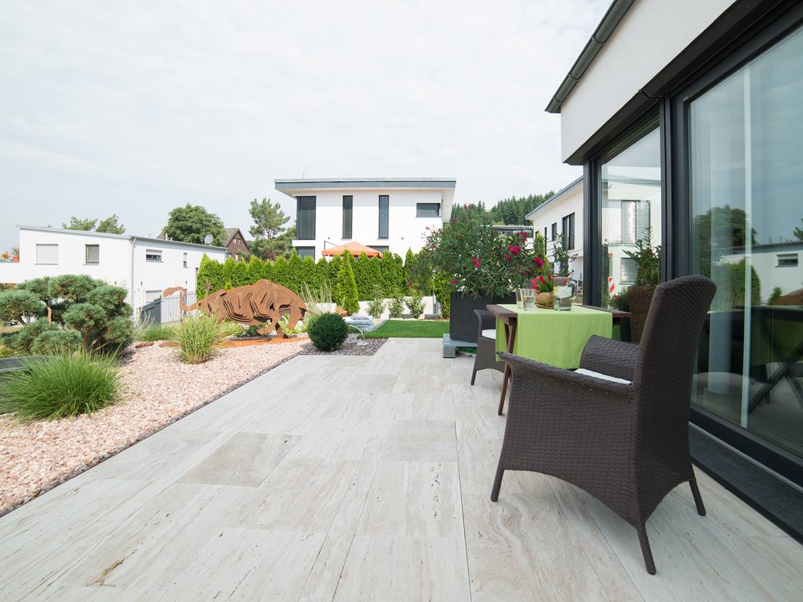 Terrasse mit modernem Steingarten und holzähnlichen Travertinplatten als Bodenbelag
