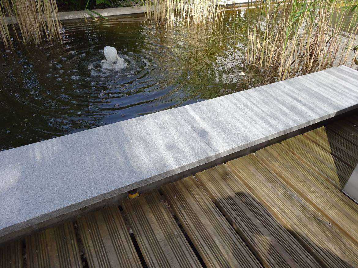 Teichbegrenzung aus Granitplatten, hinten Schilf und kleiner Springbrunnen, vorne Holzdielen