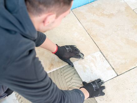Ein Fliesenleger legt eine Travertinfliese in das Kleberbett