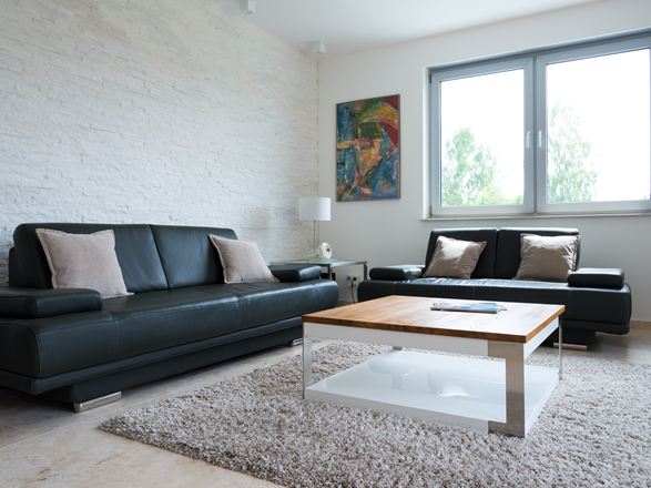 Wohnzimmer mit Naturstein-Verblendern an der Wand und einem schwarzen Sofa
