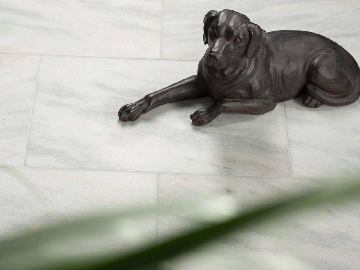 Porzellanfigur von liegendem Hund auf Marmorfliese Calacatta geschliffen